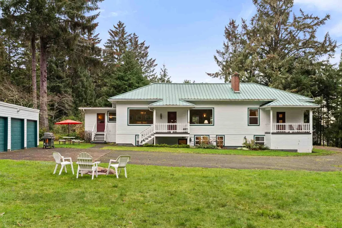 This exterior shows the house’s facade with a green roof, outdoor seating, and is framed by lush trees. The ample yard and open sky set the scene for stargazing or gathering with friends and family in privacy after a day of coastal fun.