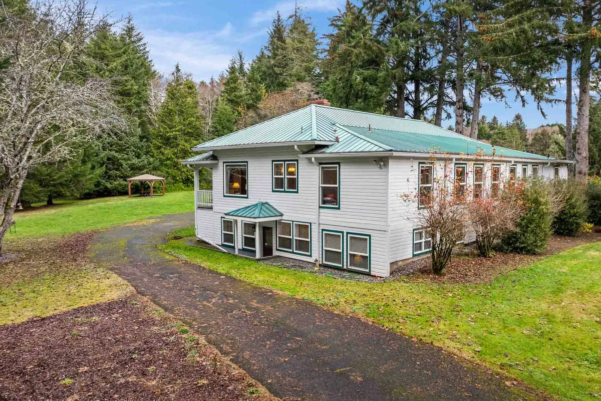 An exterior shot of the Schoolhouse, nestled among tall trees with a welcoming pathway leading to the entrance. The peaceful garden setting suggests a relaxing environment, while glimpses of the porch hint at spaces for unwinding after a day out.