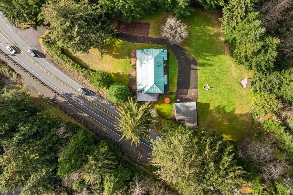 An expansive view of the house’s garden and surrounding landscape. The image captures the building, lush greenery, a quiet road, and a cozy seating area shaded by trees, suggesting opportunities for outdoor relaxation and neighborhood exploration.