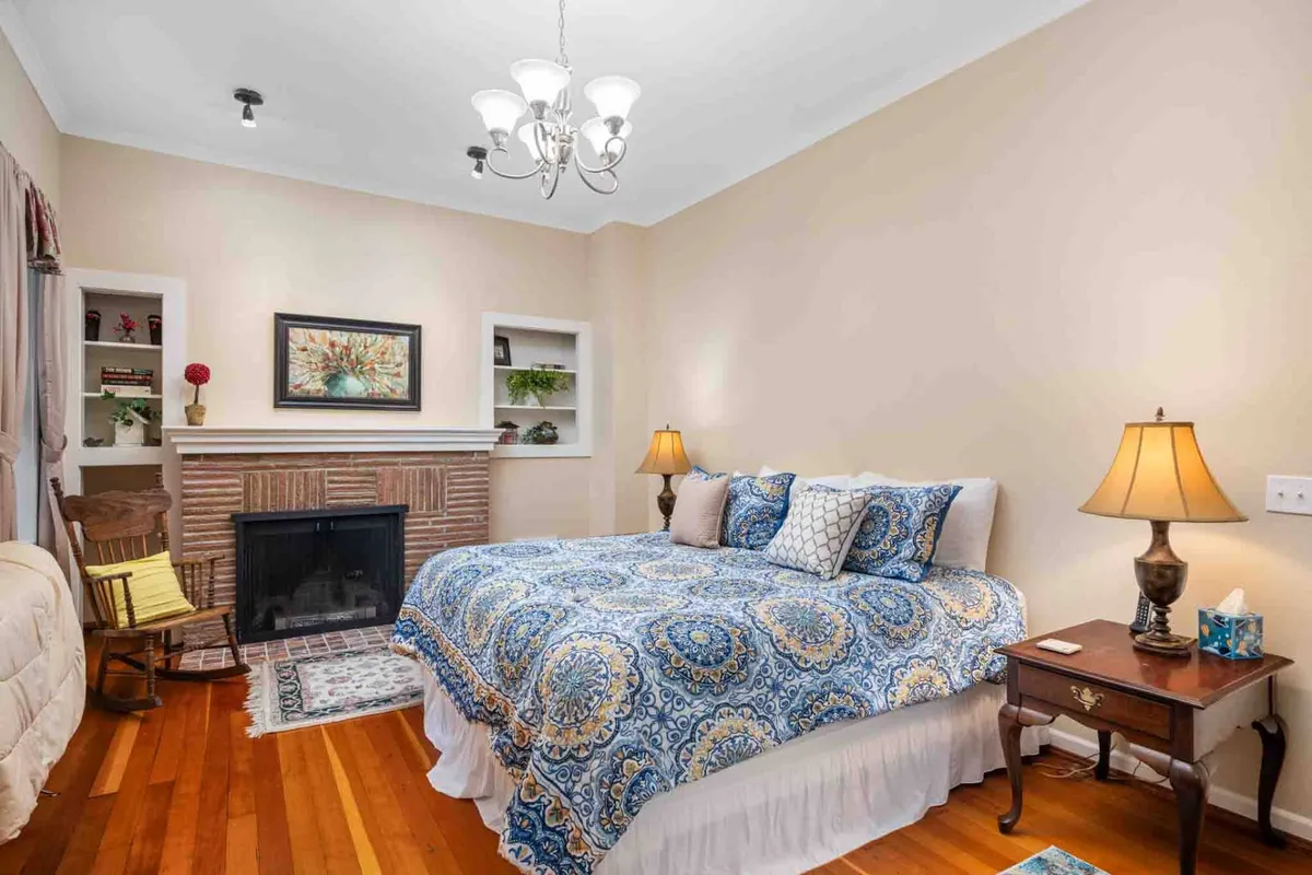A serene bedroom featuring a bed with blue patterned bedding, a cozy fireplace, and a nightstand with a lamp. The atmosphere is calm and inviting, ideal for unwinding after a long day.