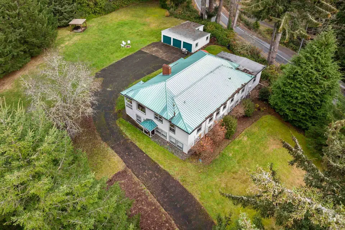 A wide shot of the large house with a green roof, expansive yard, garage, and mature trees. The generously sized, open green space is prominent, conveying the scale and privacy of the property.
