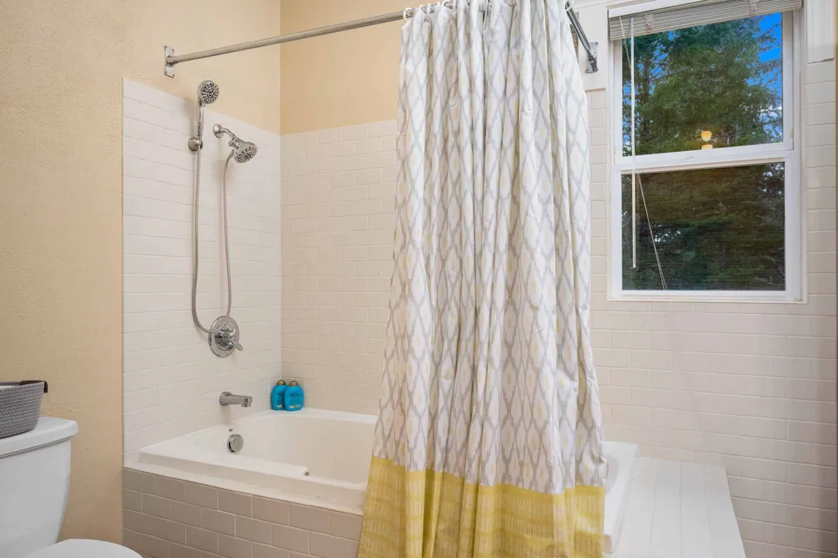 A tranquil bathroom scene featuring a bathtub with a showerhead, a soft shower curtain, and a window letting in natural light. The atmosphere is peaceful, perfect for relaxation and self-care.